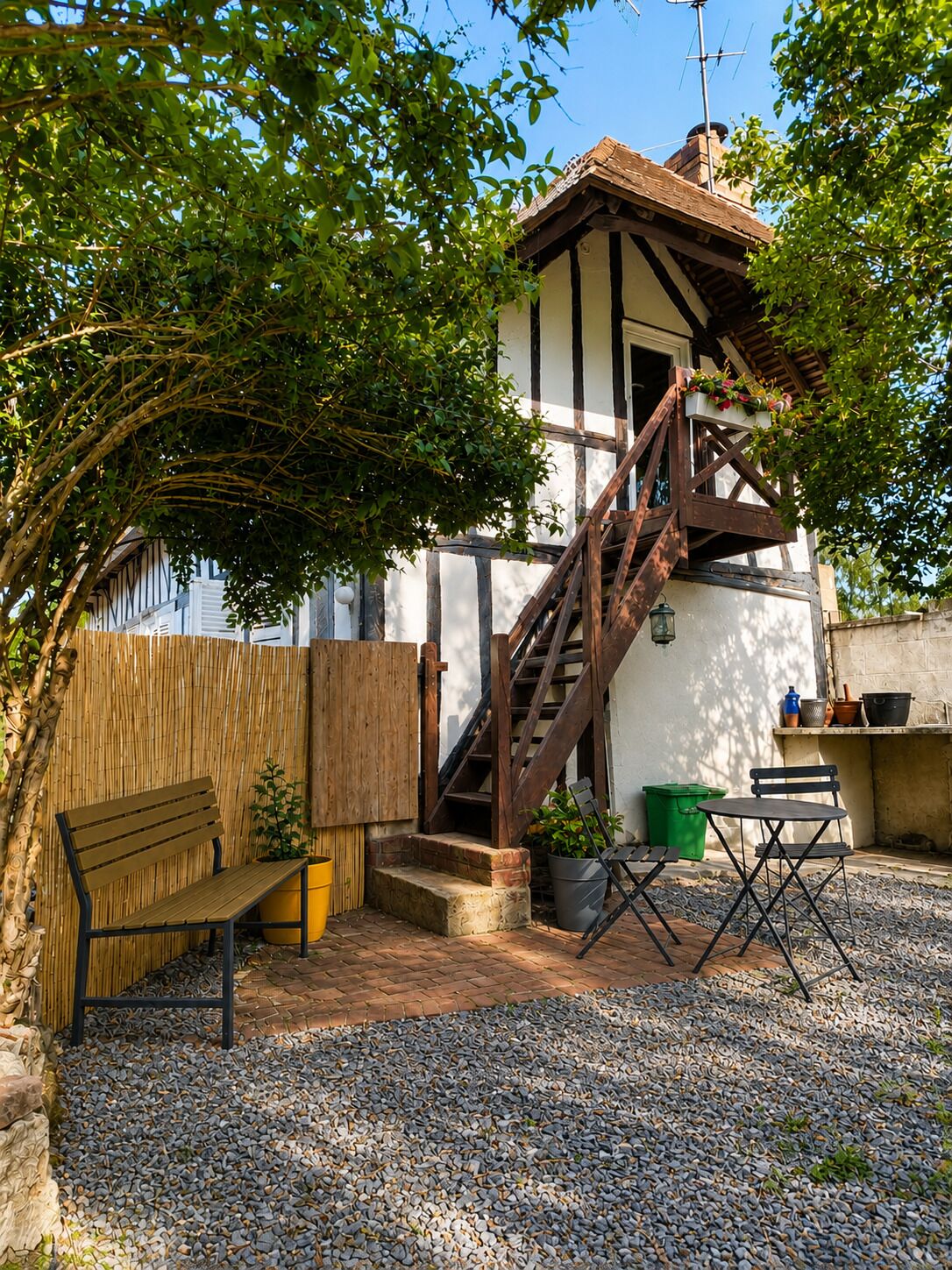 Une maison traditionnelle avec un escalier en bois menant à un balcon, un banc et un petit espace de détente extérieur.
