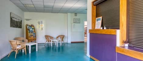 A reception area with a purple counter, wicker chairs, a small table, and a bulletin board with various notices.
