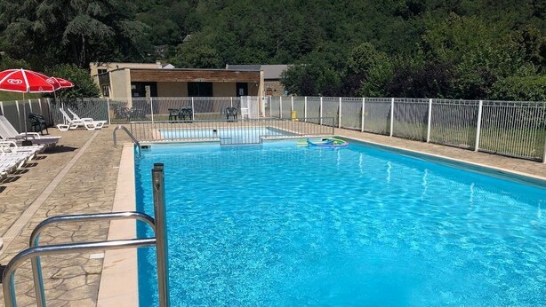 A swimming pool with a metal ladder, lounge chairs, and a fenced area with a building in the background. - À 200 m de la plage ! Balcon privé + accès piscine (Miremont)