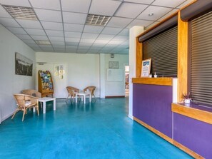 A reception area with a purple counter, wicker chairs, a small table, and a bulletin board with various notices. - À 200 m de la plage ! Balcon privé + accès piscine (Miremont)
