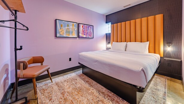 A modern hotel room with a large bed, a chair, a coat rack, and two framed pictures on the wall. - Sleep40 28Beds 10BR Super Stays A12 Low W DD (Louisville)
