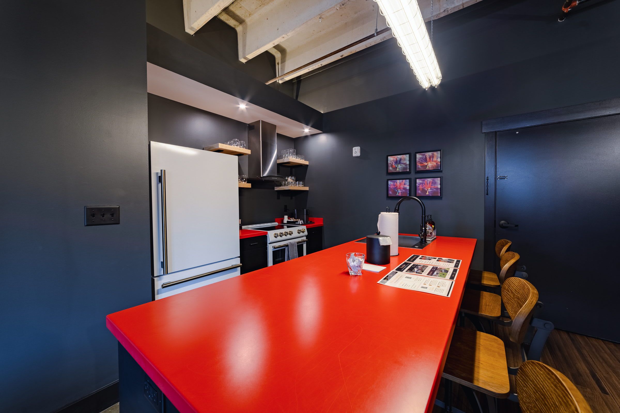 A modern kitchen with a red countertop, stainless steel appliances, and wooden chairs.