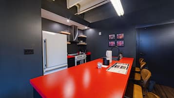 A modern kitchen with a red countertop, stainless steel appliances, and wooden chairs.