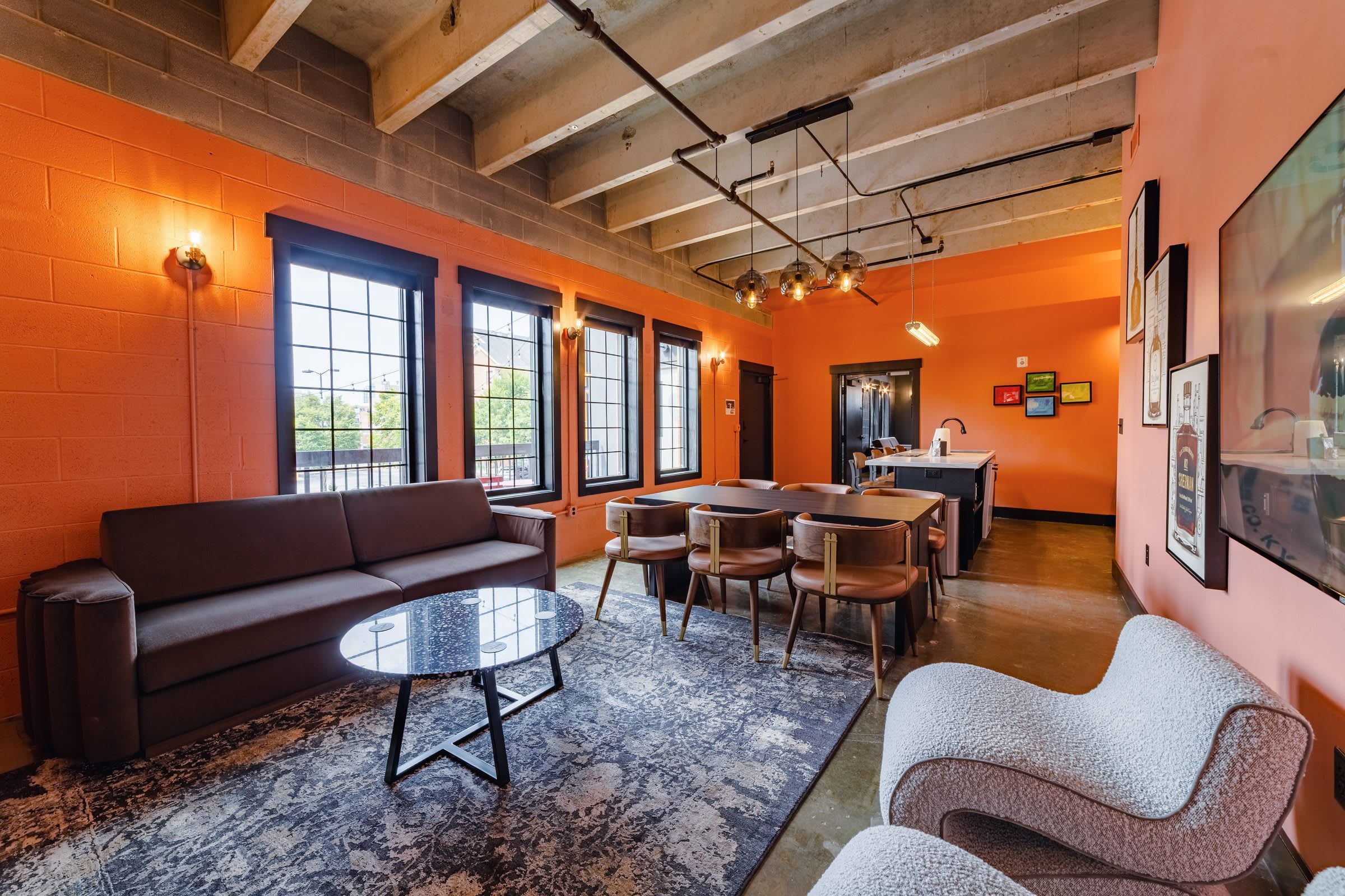 A modern lounge area with a sofa, round table, and chairs, featuring large windows and a high ceiling.