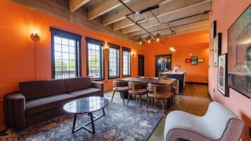 A modern lounge area with a sofa, round table, and chairs, featuring large windows and a high ceiling.