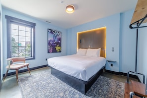 Une chambre moderne avec un grand lit, une chaise, une fenêtre et une œuvre d’art murale originale.