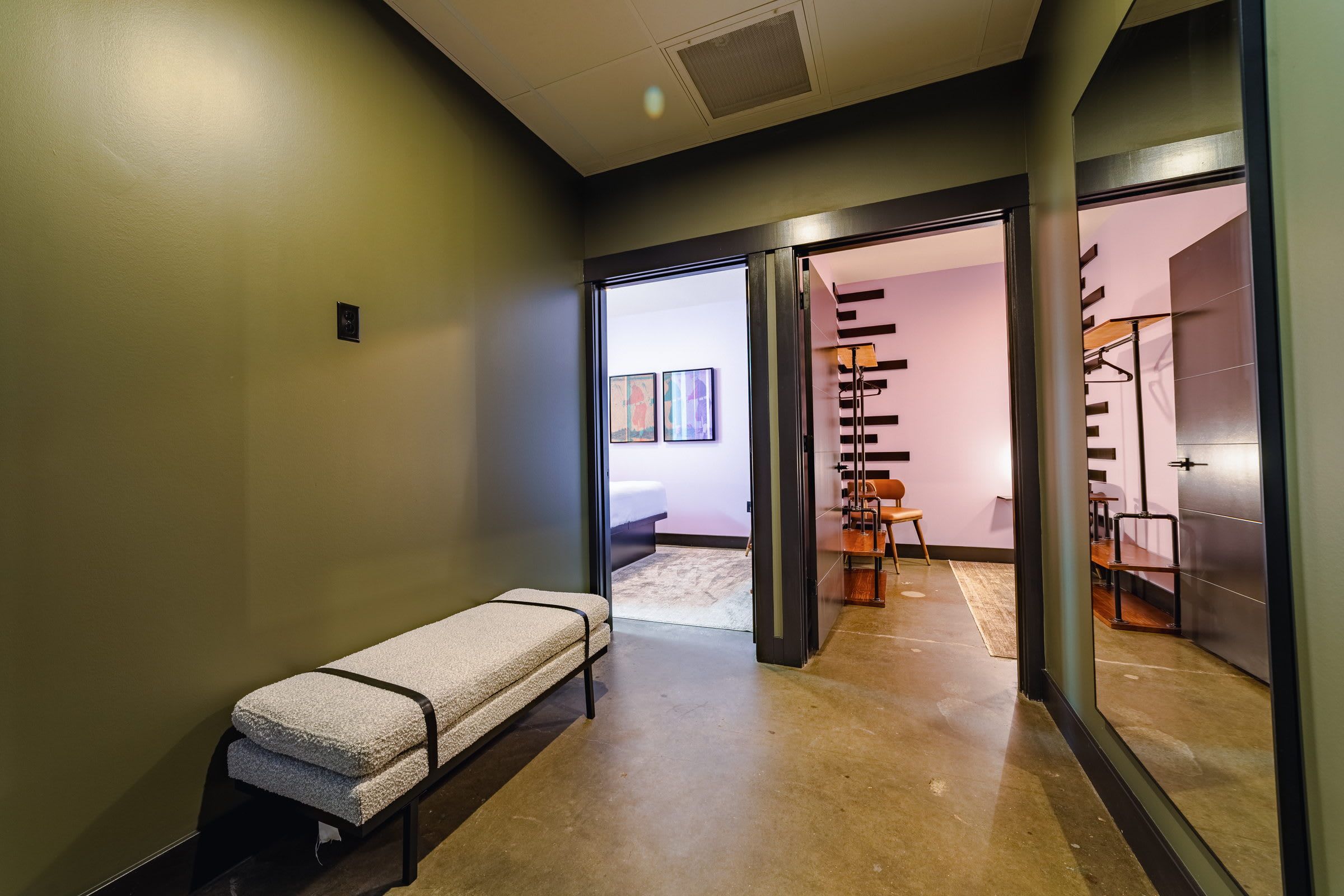 A hallway with a bench, a door leading to a room with a bed, and a staircase.