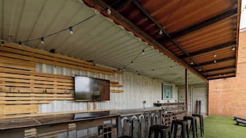 An outdoor bar area with a long counter, wooden slats, and a television mounted on the wall.