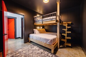 A bunk bed room with a wooden ladder, a red door, and a patterned rug.