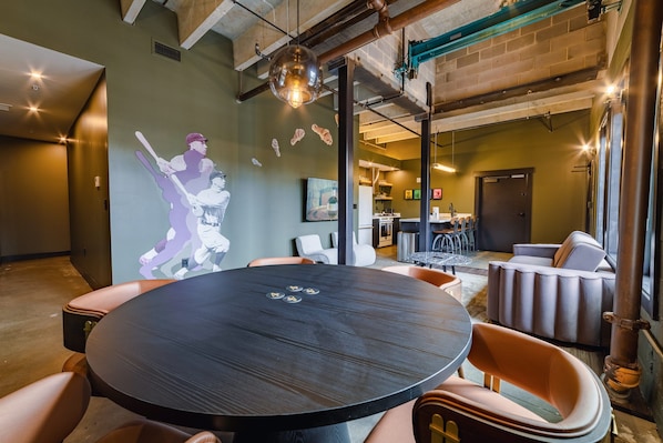 A modern lounge area with a round table, leather chairs, and a wall-mounted projector screen displaying a baseball player.