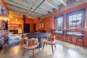 A modern interior with a round table and chairs, a kitchen area, and large windows with a view of the street.
