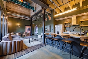 Un área de bar moderna con taburetes, una barra y un espacio de estar con un sofá y mesas.