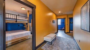 A hotel room with a bunk bed, a small seating area, and a hallway leading to another room.
