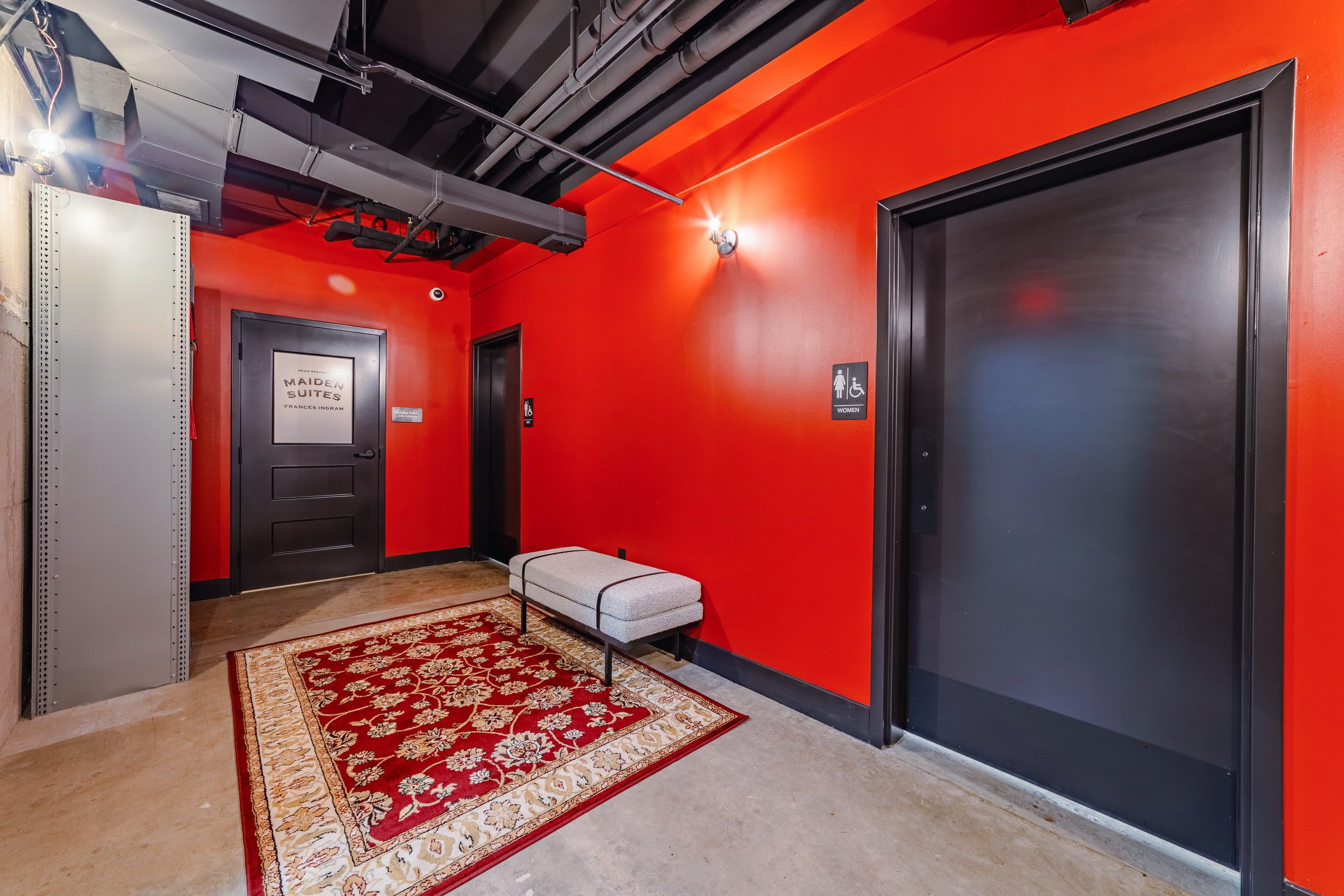 A hallway with a red carpet, a bench, and a door marked 'WOMEN'.