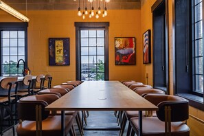 Uma sala de conferências com uma mesa comprida e cadeiras de couro, amplas janelas e obras de arte nas paredes.