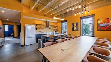 A modern kitchen with a long dining table and chairs, a refrigerator, and a window with a view.