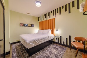 A hotel room with a bed, a chair, a rug, a wall with pictures, and a ceiling light. - Sleep46 23Beds 16BR Super Stays A12 Up Pad Stretch (Louisville)