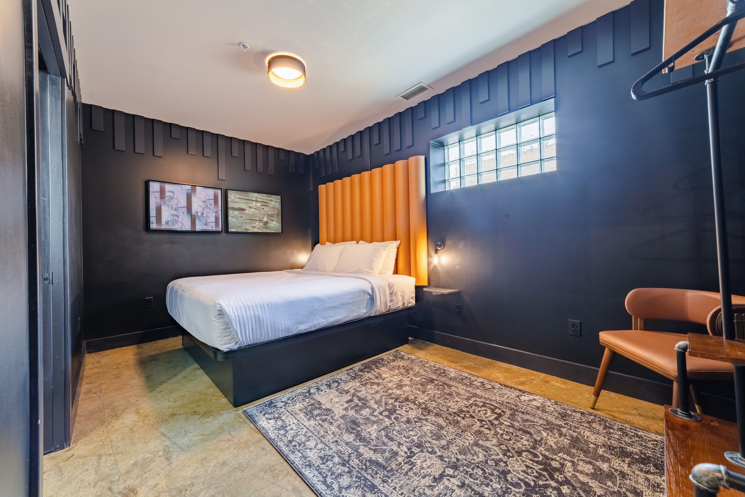 A modern bedroom with a bed, a chair, a rug, and artwork on the wall.