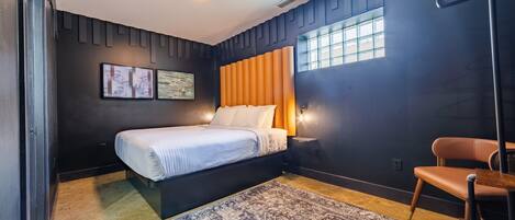 A modern bedroom with a bed, a chair, a rug, and artwork on the wall.