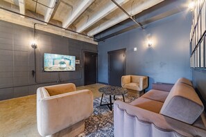 Ein moderner Loungebereich mit großem Flachbildfernseher an der Wand, einer Couch, einem Sessel und einem Couchtisch.