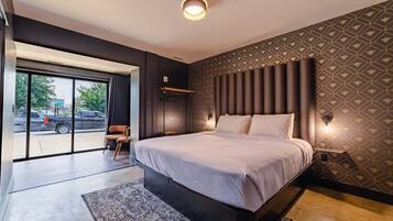 A modern bedroom with a large bed, a view of the street through a glass door, and a patterned wall.