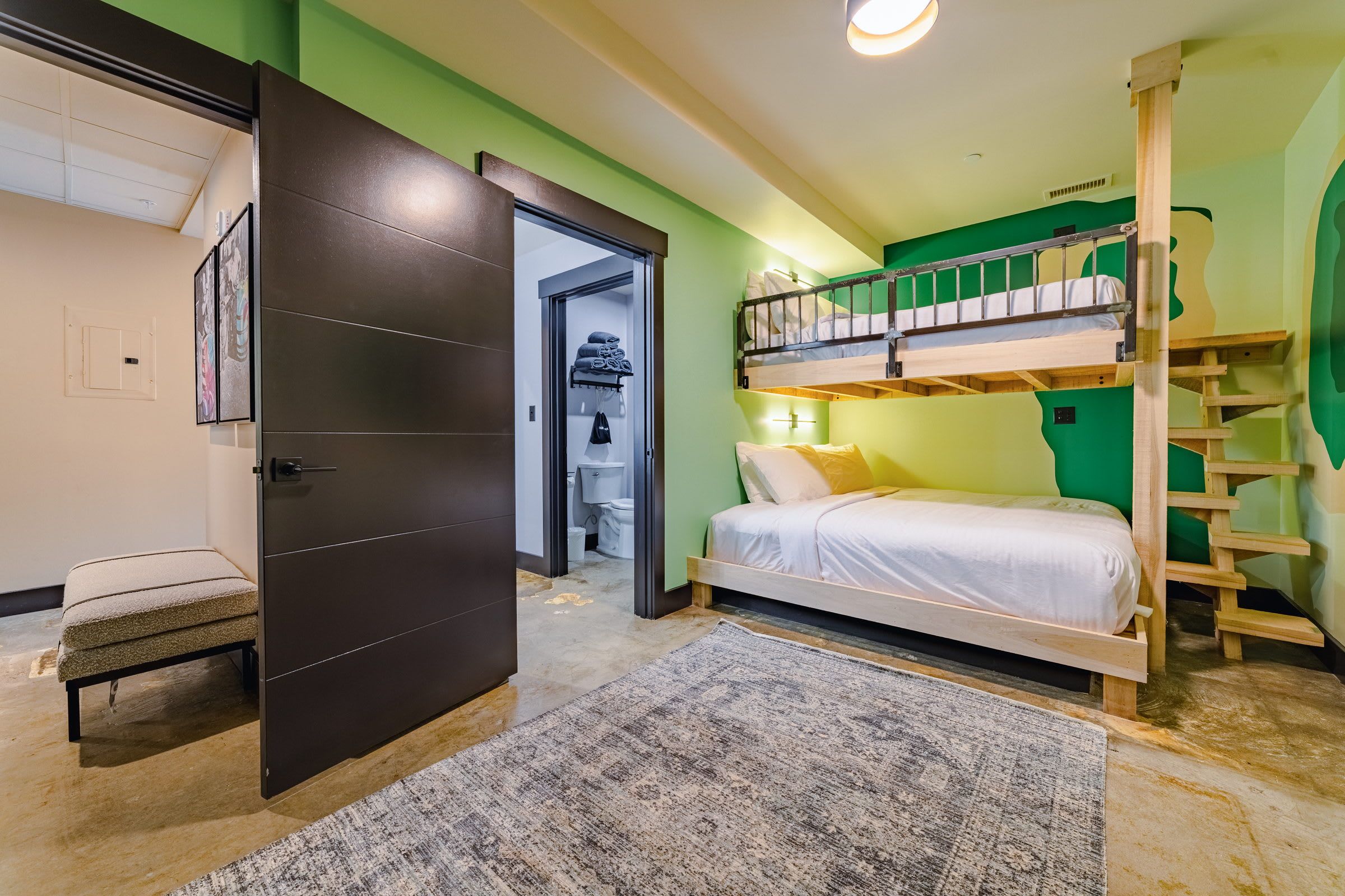 Una habitación con literas, una puerta que da al baño y una pequeña banca.