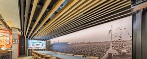 Un salón de conferencias con una larga mesa y sillas, una pantalla grande y un mural de un evento concurrido.