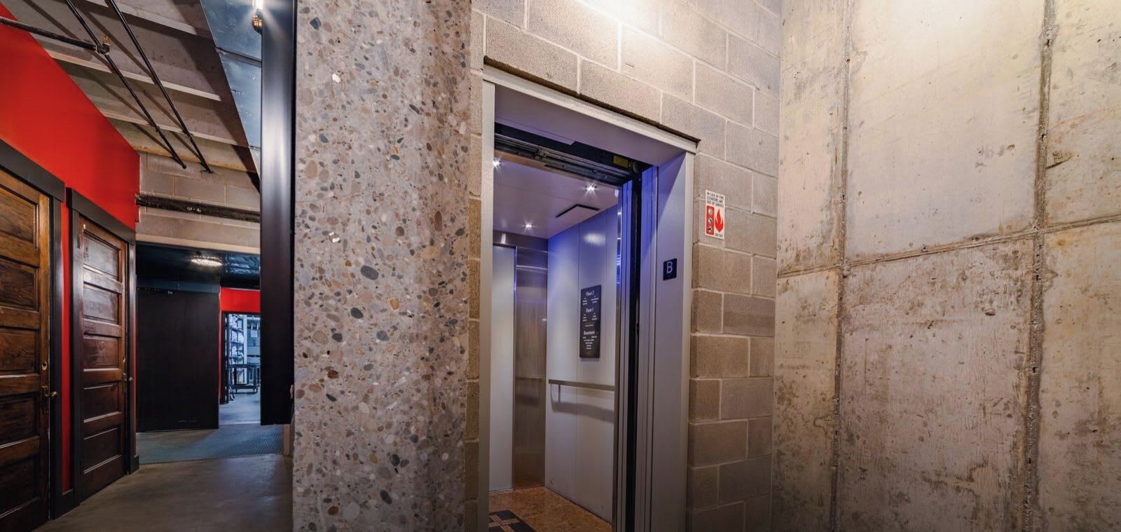 An elevator with a sign indicating the floor level, a fire safety sign, and a corridor with a red wall and a door.