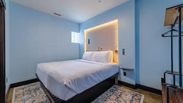 Une chambre à coucher avec un lit, une table de chevet, une lampe fixée au mur et un tapis à motifs.