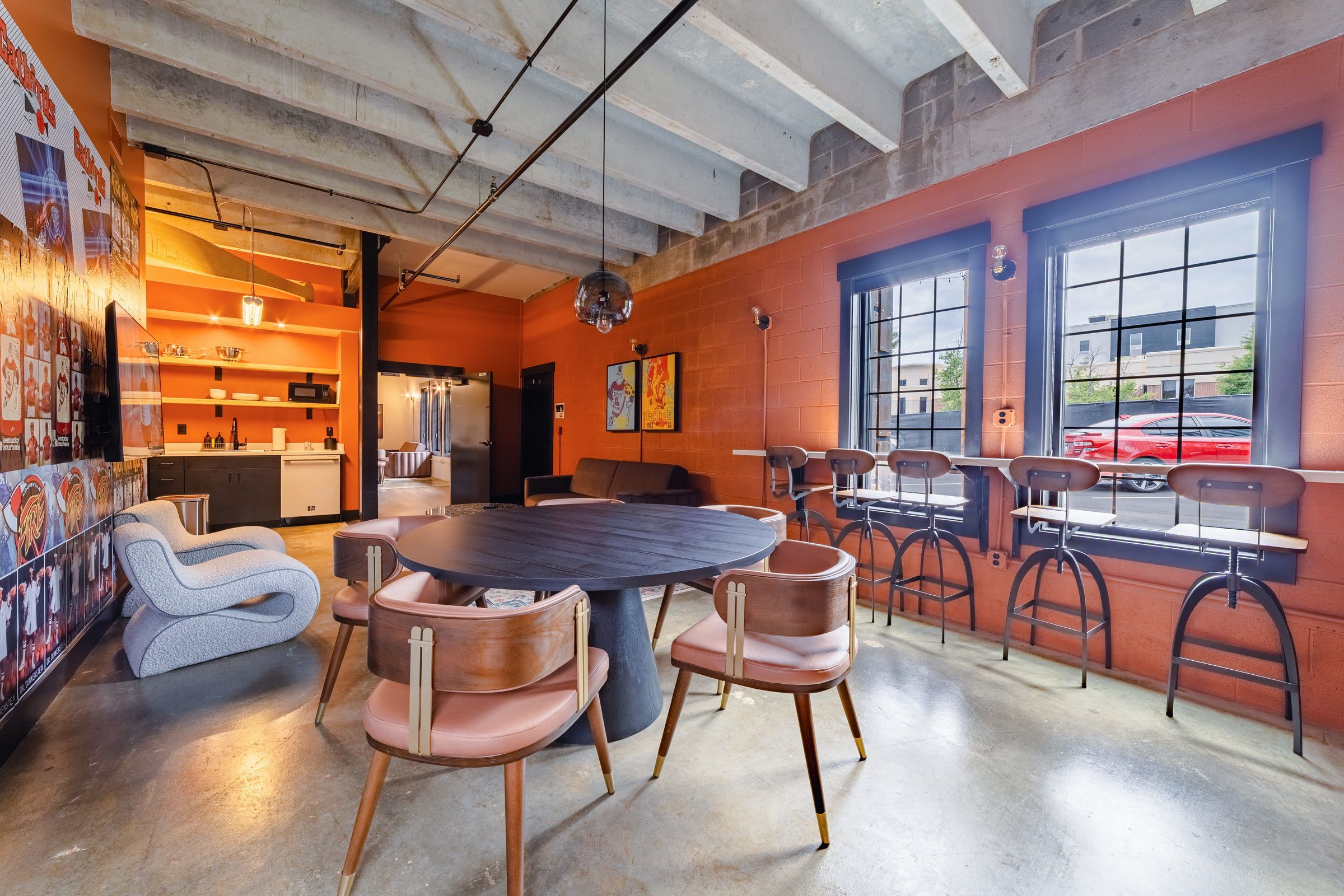 A modern dining area with a round table and chairs, a kitchen in the background, and large windows with a view of the street.