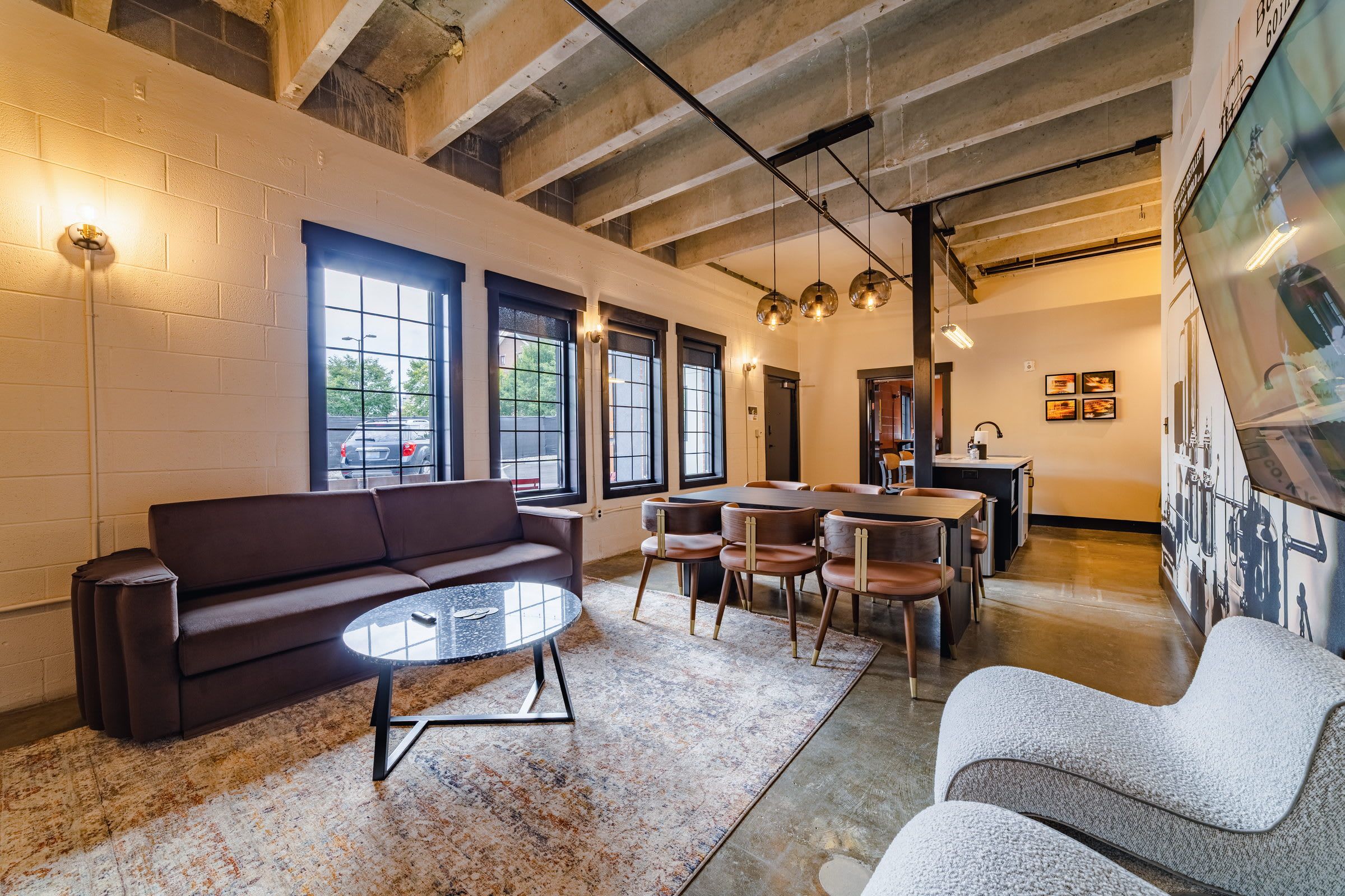 A modern interior with a sofa, round table, and chairs, a kitchen area, and large windows.