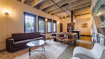 A modern interior with a sofa, round table, and chairs, a kitchen area, and large windows.