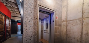 An elevator with a sign indicating the floor level, a fire safety sign, and a corridor with a red wall and a door.