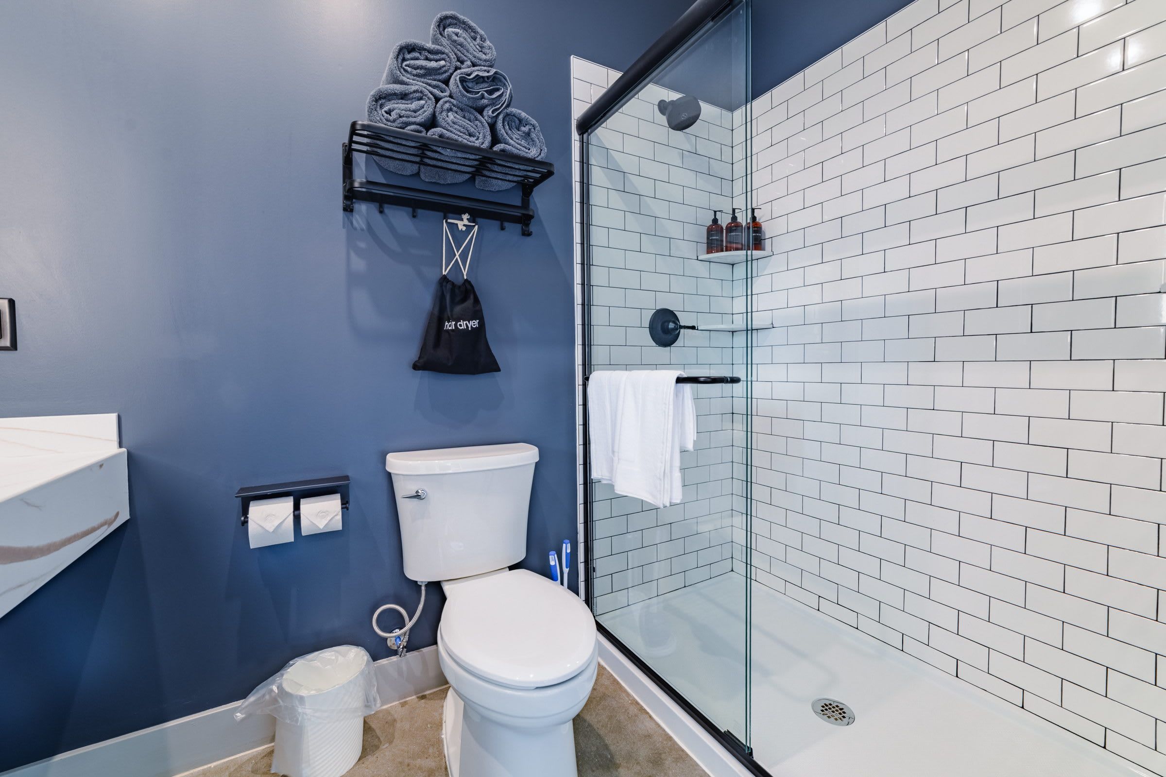 A bathroom with a glass shower enclosure, a white toilet, and a towel rack with folded towels.