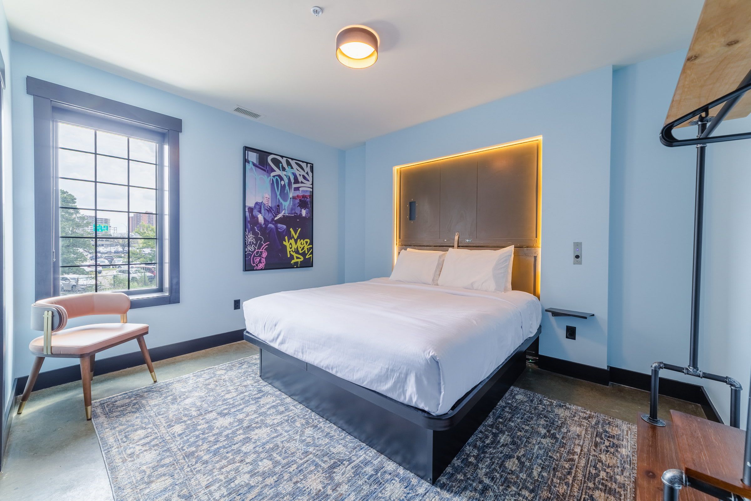 Una camera da letto moderna con un letto grande, una sedia, una finestra e un'opera d'arte originale al muro.