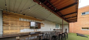 An outdoor bar area with a long counter, wooden slats, and a television mounted on the wall.