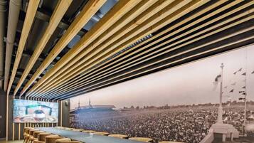 A conference room with a long table, chairs, and a large screen displaying a crowd.