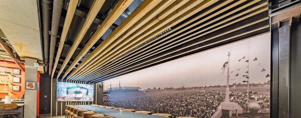 A conference room with a long table, chairs, and a large screen displaying a crowd.