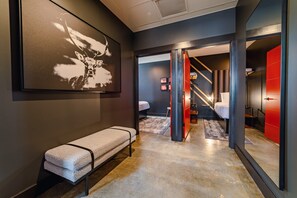 Un moderno vestíbulo de hotel con un banco, un cuadro abstracto de gran tamaño y una escalera que conduce a una zona de dormitorios.