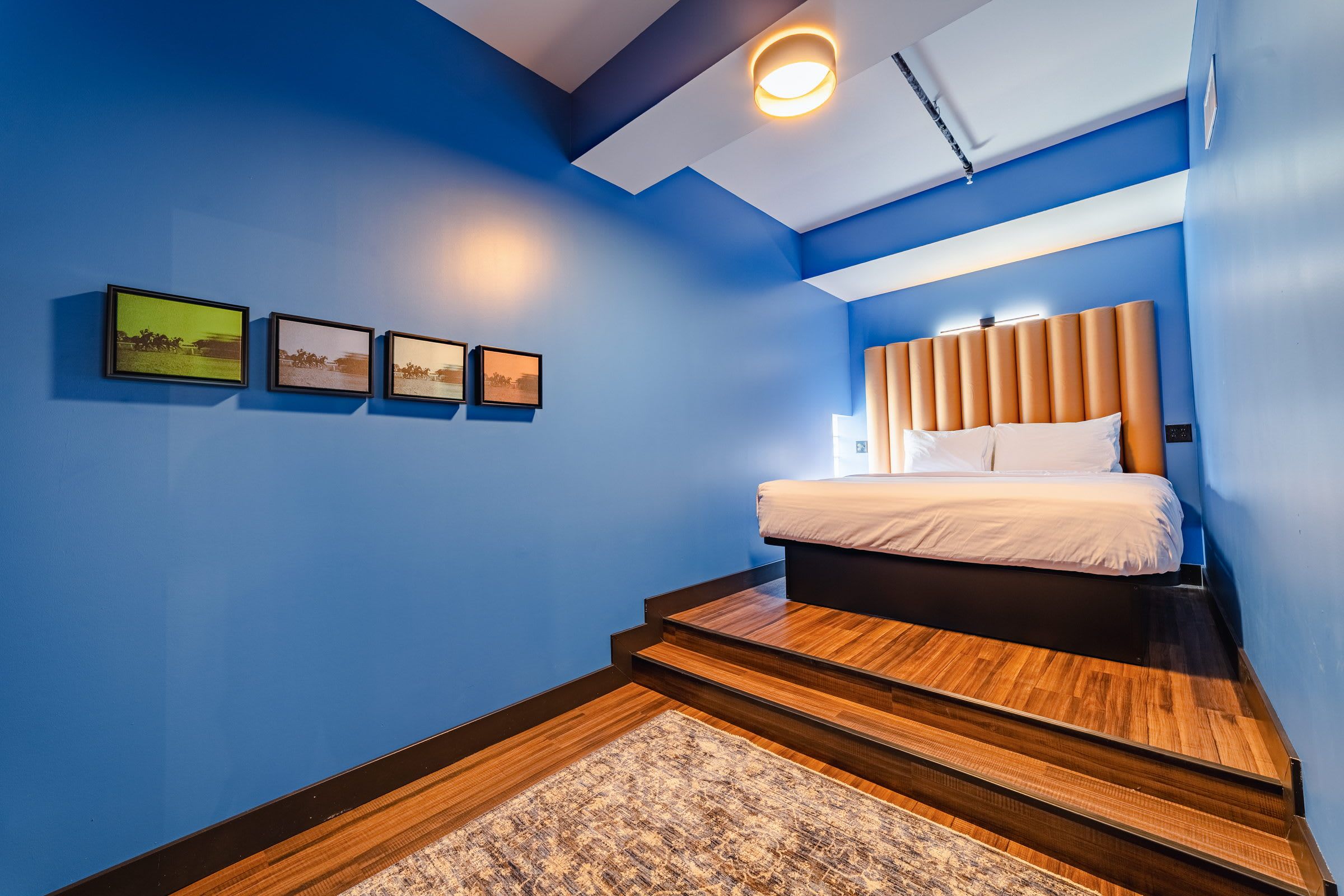 Une chambre à coucher avec un lit, une tête de lit, une lampe fixée au mur et un petit tapis.