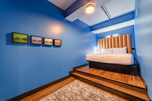 Ein Schlafzimmer mit einem Bett, einem Kopfteil, einer Wandleuchte und einem kleinen Teppich.