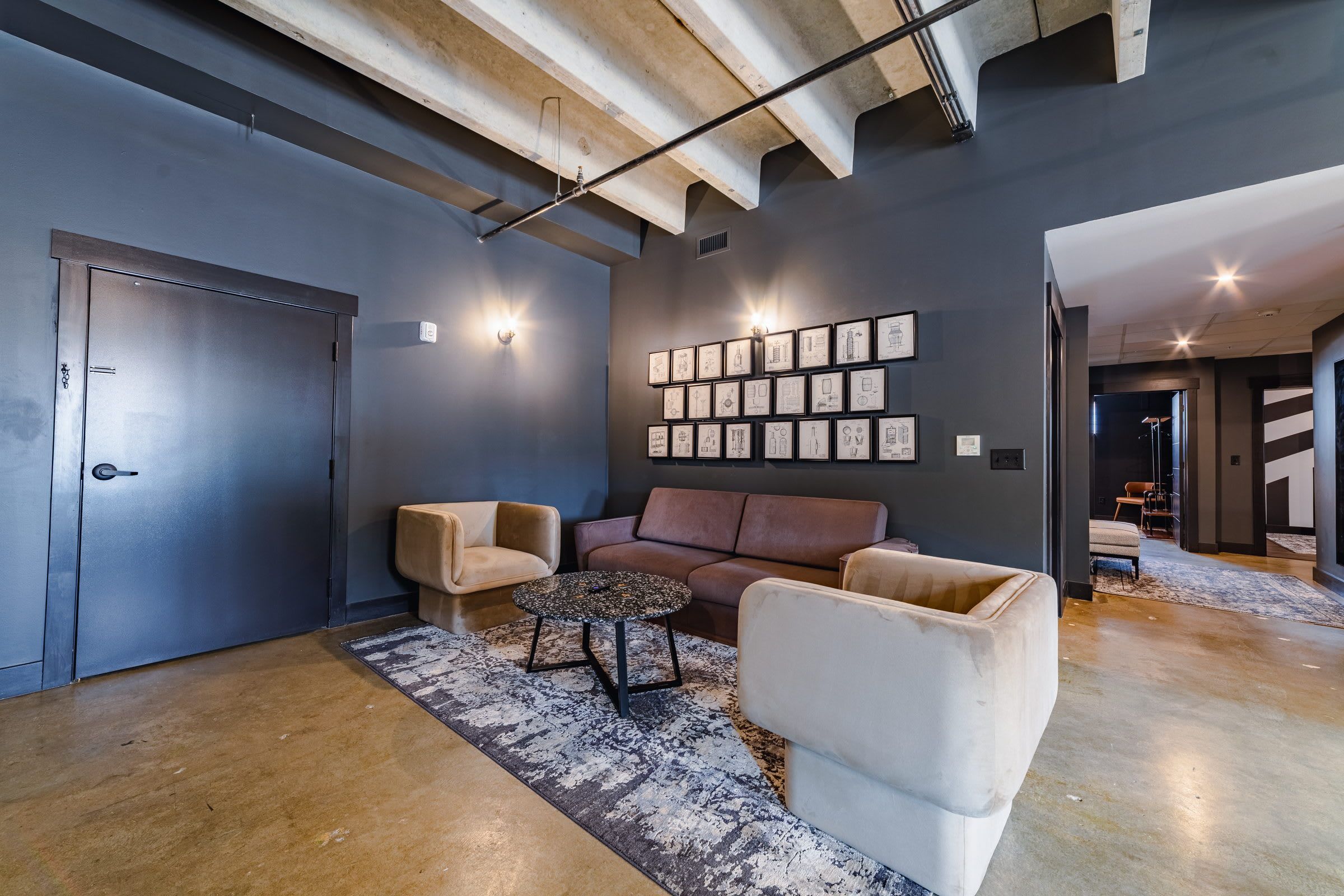 Un intérieur moderne avec un mur foncé, une porte, un canapé, une table basse et un mur décoré de tableaux encadrés.