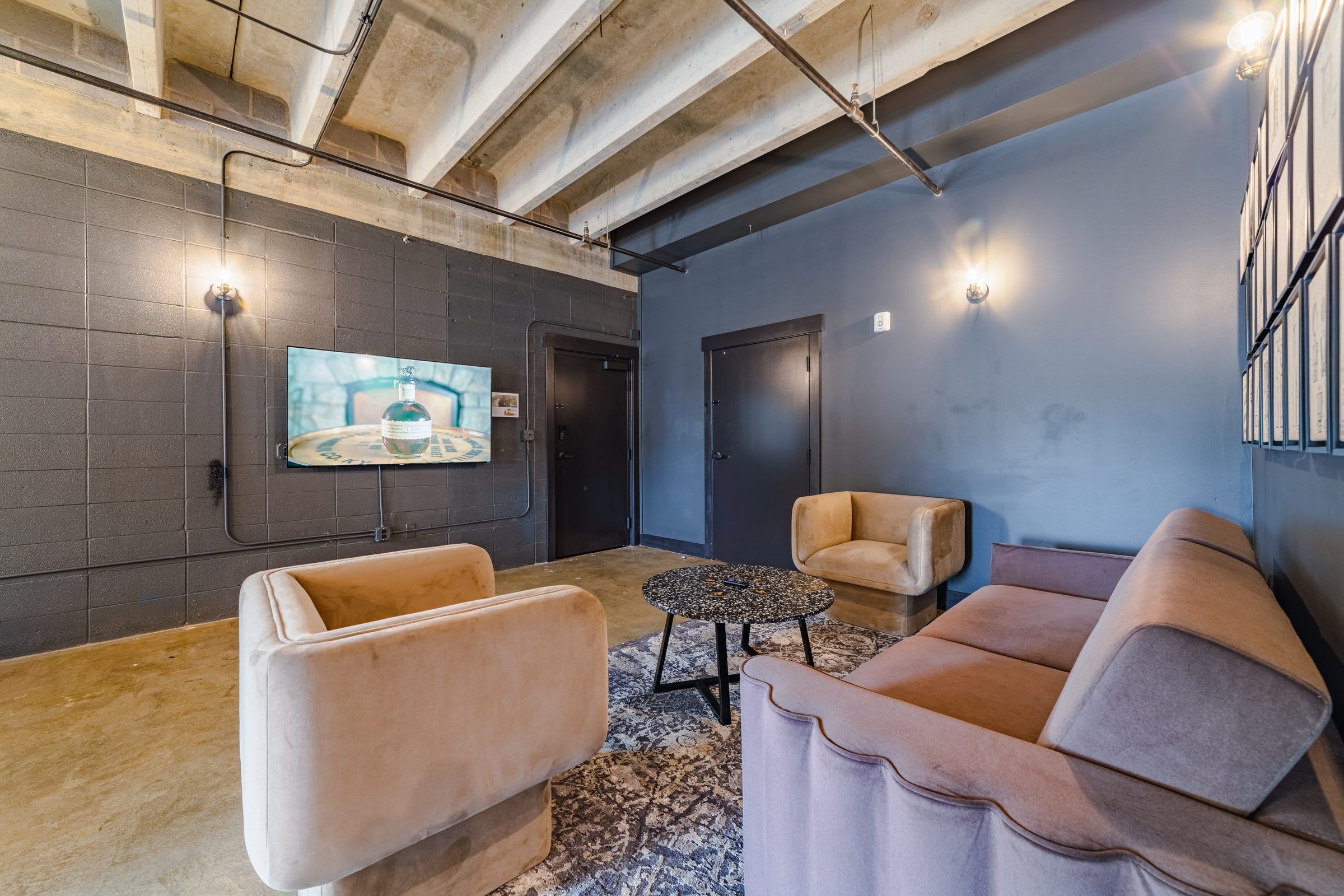 A modern lounge area with a large flat-screen TV mounted on the wall, a sofa, a smaller armchair, and a coffee table.