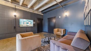 A modern lounge area with a large flat-screen TV mounted on the wall, a sofa, a smaller armchair, and a coffee table.