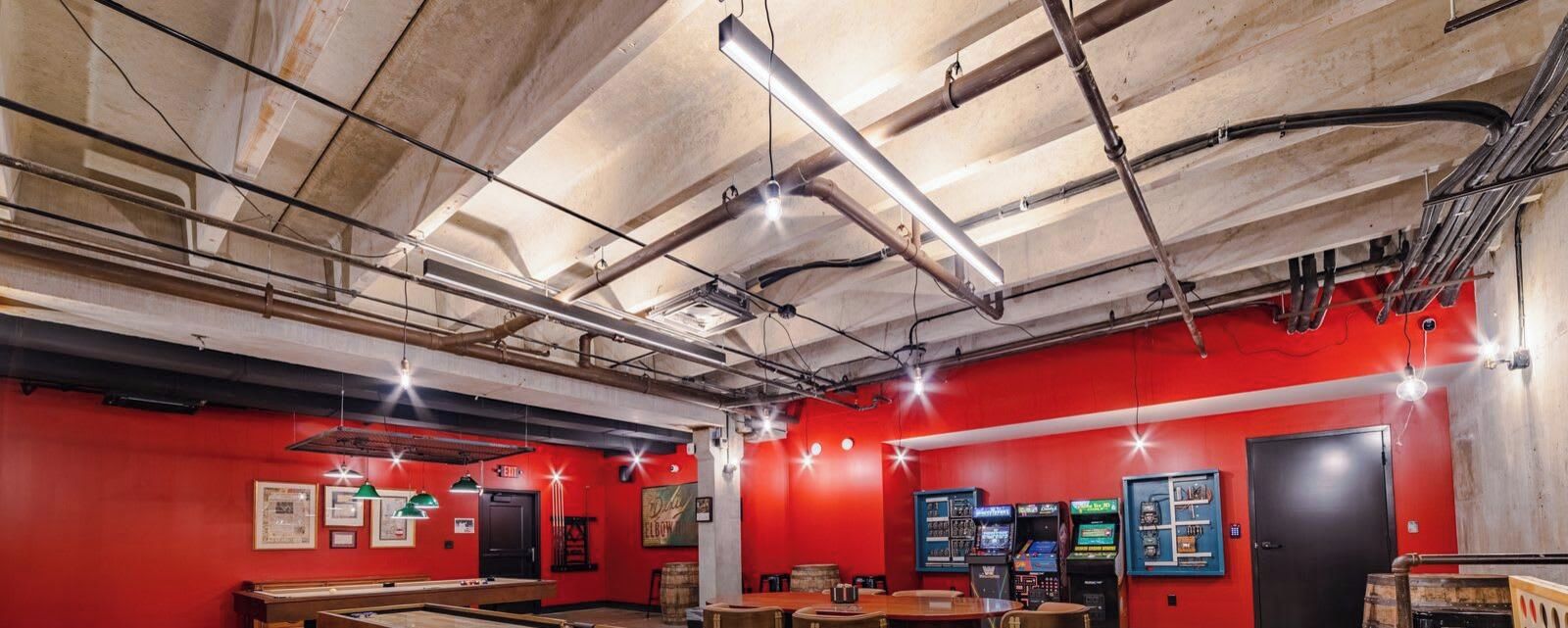 A room with red walls, exposed ceiling pipes, and a pool table.