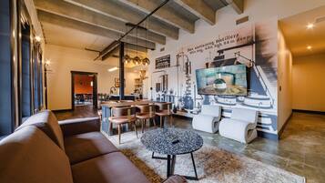 Un salon moderne comprenant un canapé, une table basse et un coin repas avec des chaises. Un grand mur est décoré d’une fresque représentant du matériel de distillerie.