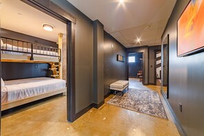 Ein modernes Hotelzimmer mit Stockbett, einer kleinen Sitzecke und einem Flur zum Badezimmer.