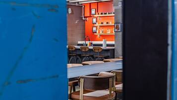 Interior de restaurante com parede de tijolos, prateleiras laranjas e cadeiras de madeira.