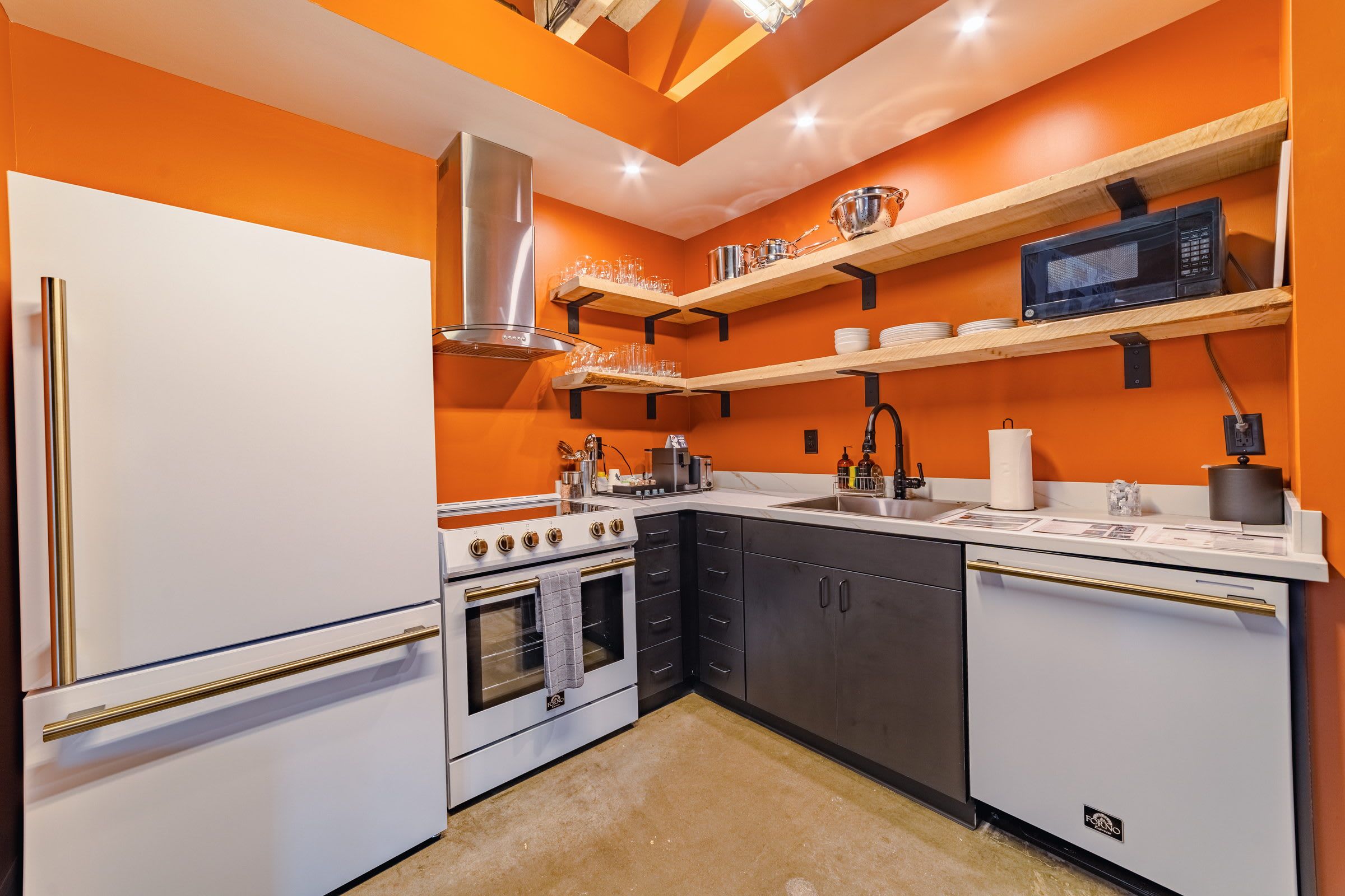 Una cocina con armarios blancos, una campana extractora de acero inoxidable y un microondas en un estante.