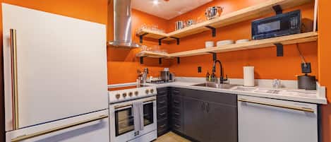 Una cocina con armarios blancos, una campana extractora de acero inoxidable y un microondas en un estante.